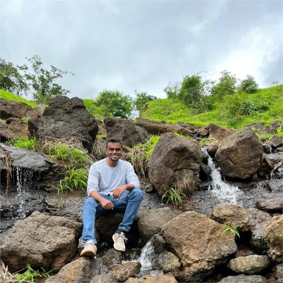 Sumeet sitting on rocks beside a waterfall on a monsoon trek in India